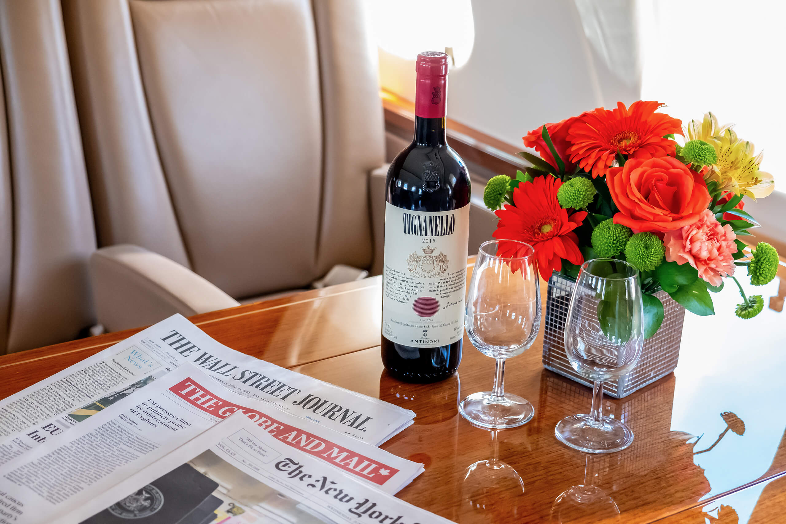 Red wine, wine glass, bouquet of flowers and newspaper on the table of a private jet.